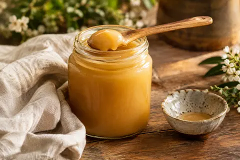 Pot de miel de thym crémeux posé sur du bois patiné avec une cuillère et un linge écru